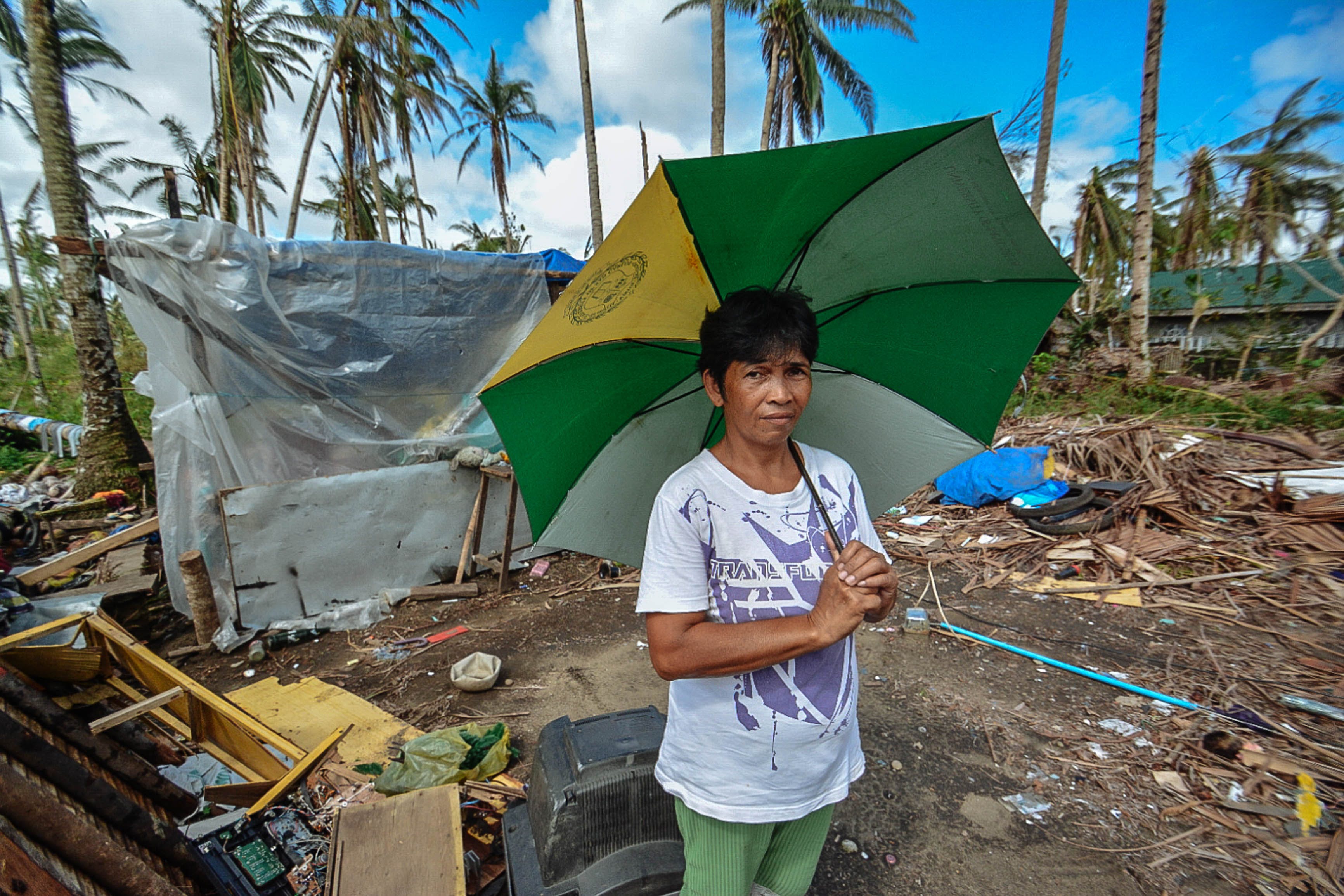 Person holding an umbrella in an area that has been damaged by a severe weather event.